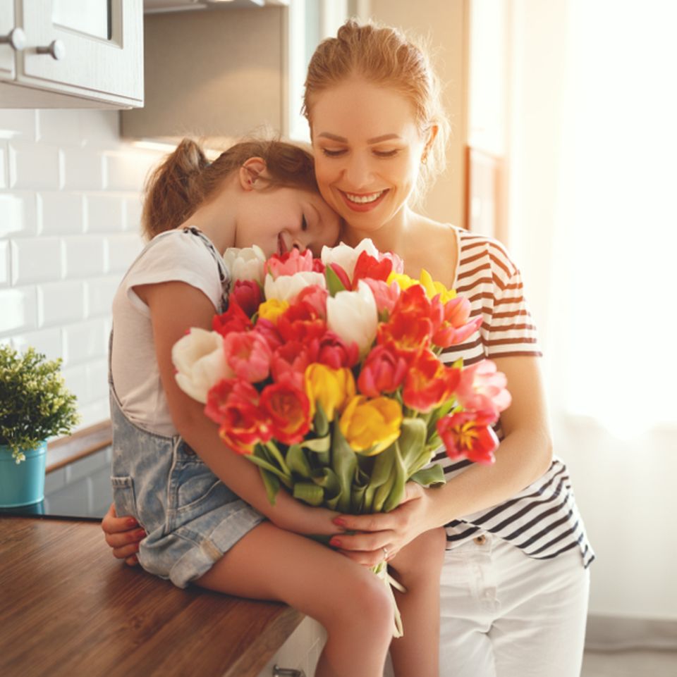 Warum feiern wir Muttertag? Tochter überreicht Blumenstrauß an Mama