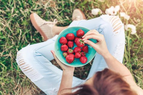 Kann Essen wirklich heilen: Frau isst Erdbeeren auf einer Wiese