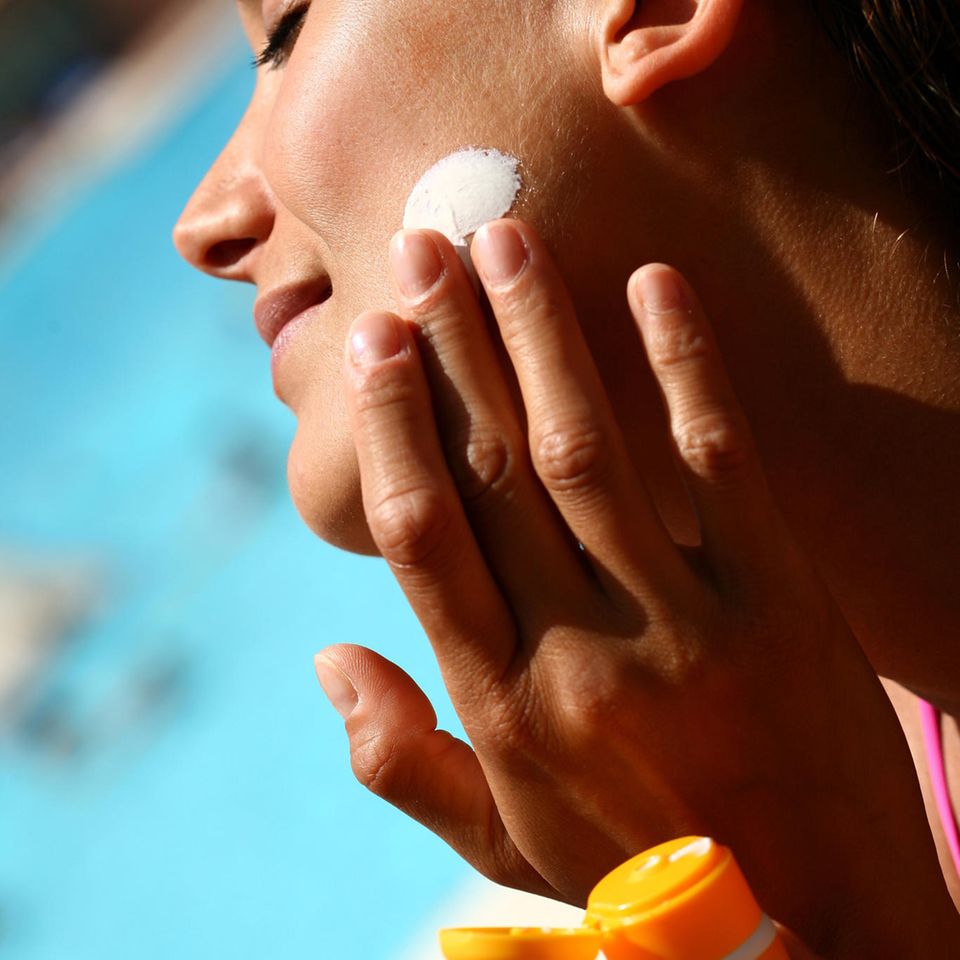 Sonnencreme fürs Gesicht: Frau cremt sich mit Sonnencreme im Gesicht ein