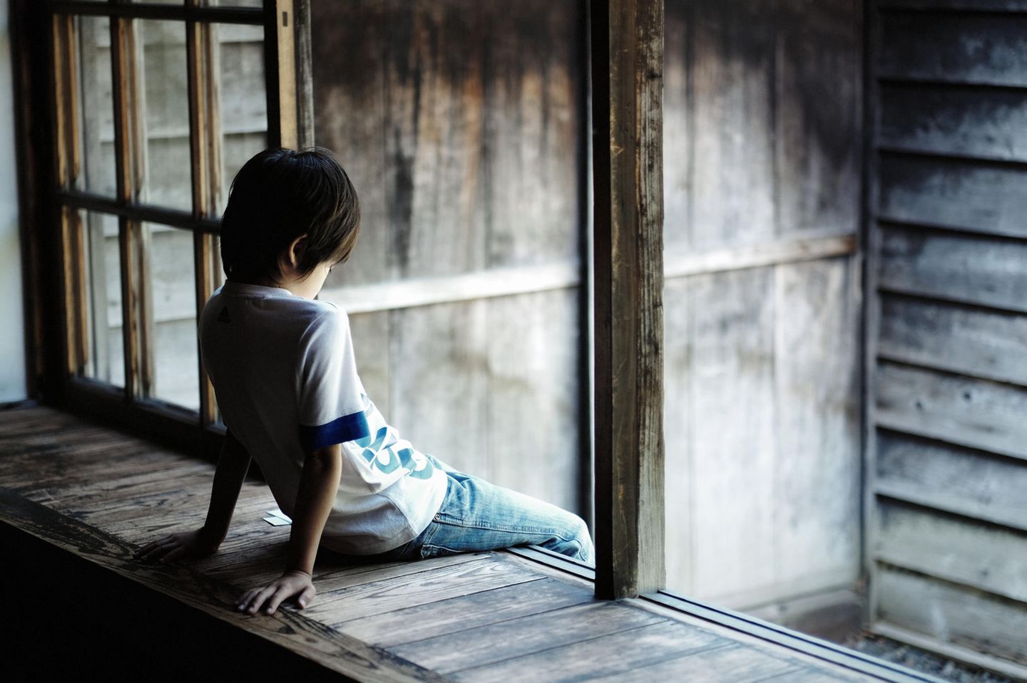Studie: Ein deprimierter kleiner Junge mit gesenktem Kopf am Fenster