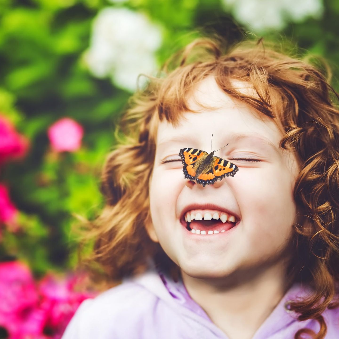 Ein lachendes kleines Mädchen mit einem Schmetterling auf der Nase