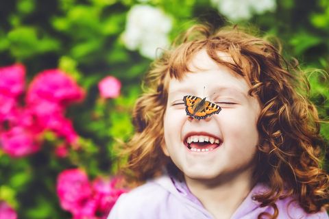 Ein lachendes kleines Mädchen mit einem Schmetterling auf der Nase