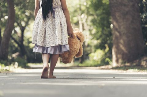 Lieblose Kindheit: Mädchen läuft barfuß auf der Straße und hält Teddy