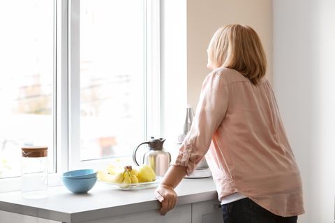 Empty Nest Syndrom: Einsame Frau steht in der Küche und sieht aus dem Fenster