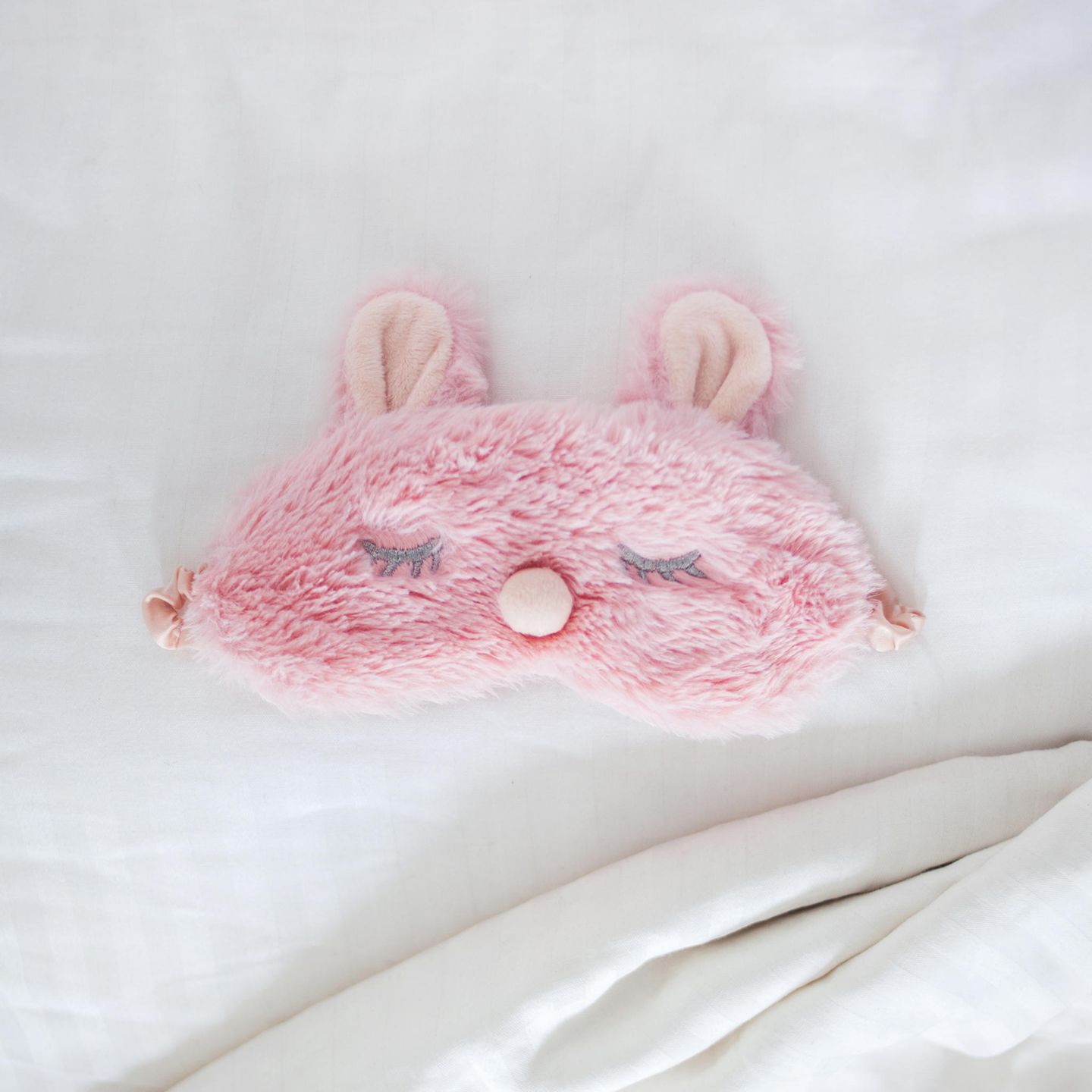 Gesund leben: Rosa Schlafmaske aus Plüsch auf einem Bett
