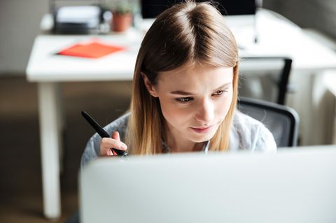 Konzentriert arbeiten: Junge Frau schaut auf Computer-Monitor