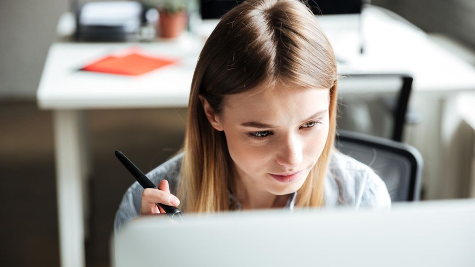 Konzentriert arbeiten: Junge Frau schaut auf Computer-Monitor