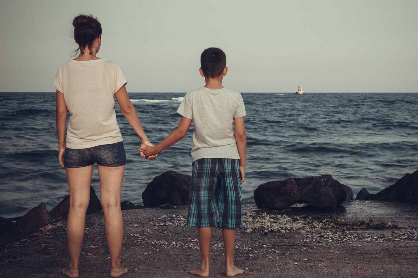 Angela Rose: Eine Frau und ihr Sohn schauen aufs Meer und halten sich an den Händen