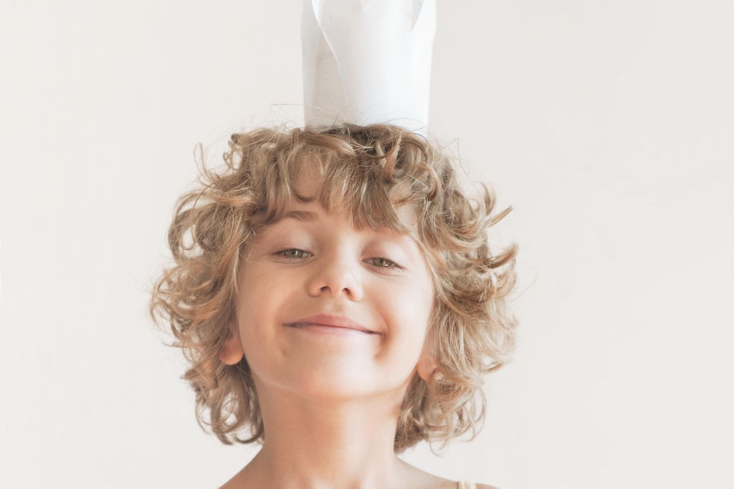 Kinder zu viel loben: Ein kleiner gelockter Junge mit Papierkrone auf dem Kopf