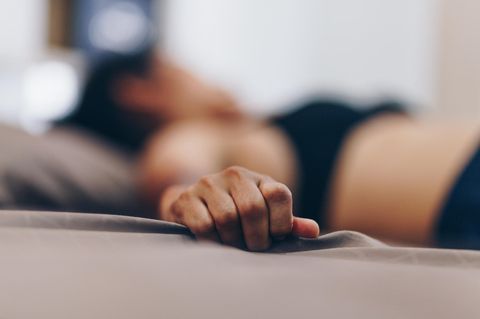 Orgasmusprobleme – eine verkrampfte Frau greift ins Laken