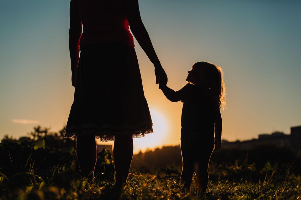 Mutter mit Asperger-Syndrom: Mutter und Kind halten vor einem Sonnenuntergang Händchen