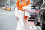 Frau mit weißer Hose, weißer Jacke und Rollkragenpullover in Orange