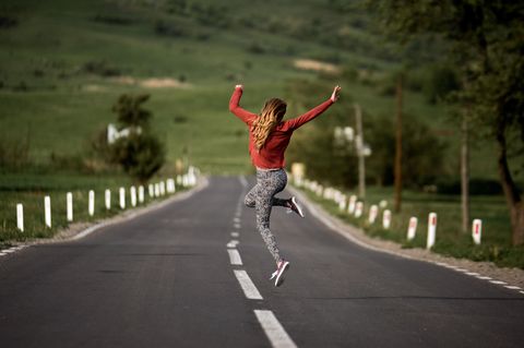 Gewohnheiten ändern: Frau auf Landstraße springt in die Luft