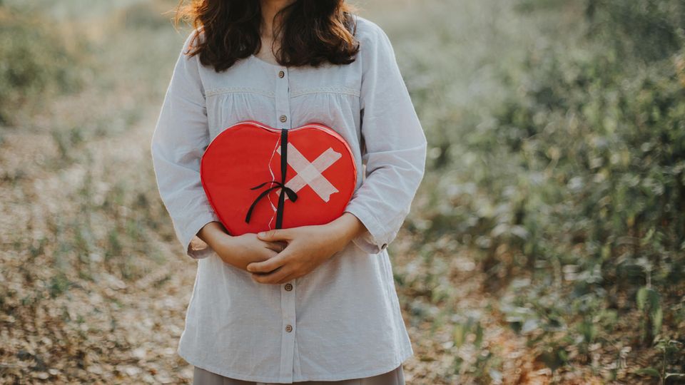 Tipps für Menschen mit gebrochenem Herzen: Eine Frau hält ein rotes Herz mit Pflaster vor den Bauch