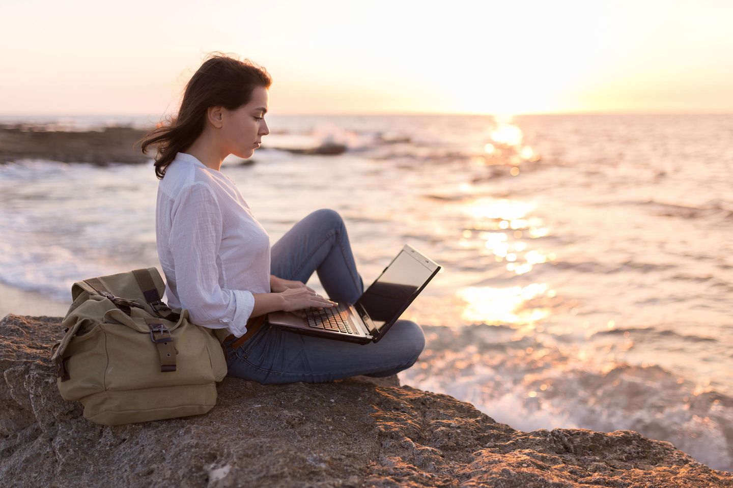 Jobpause: Frau sitzt mit Laptop am Meer