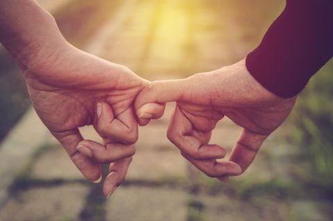 7 eindeutige Zeichen der Liebe: Mann und Frau halten einander an den kleinen Fingern