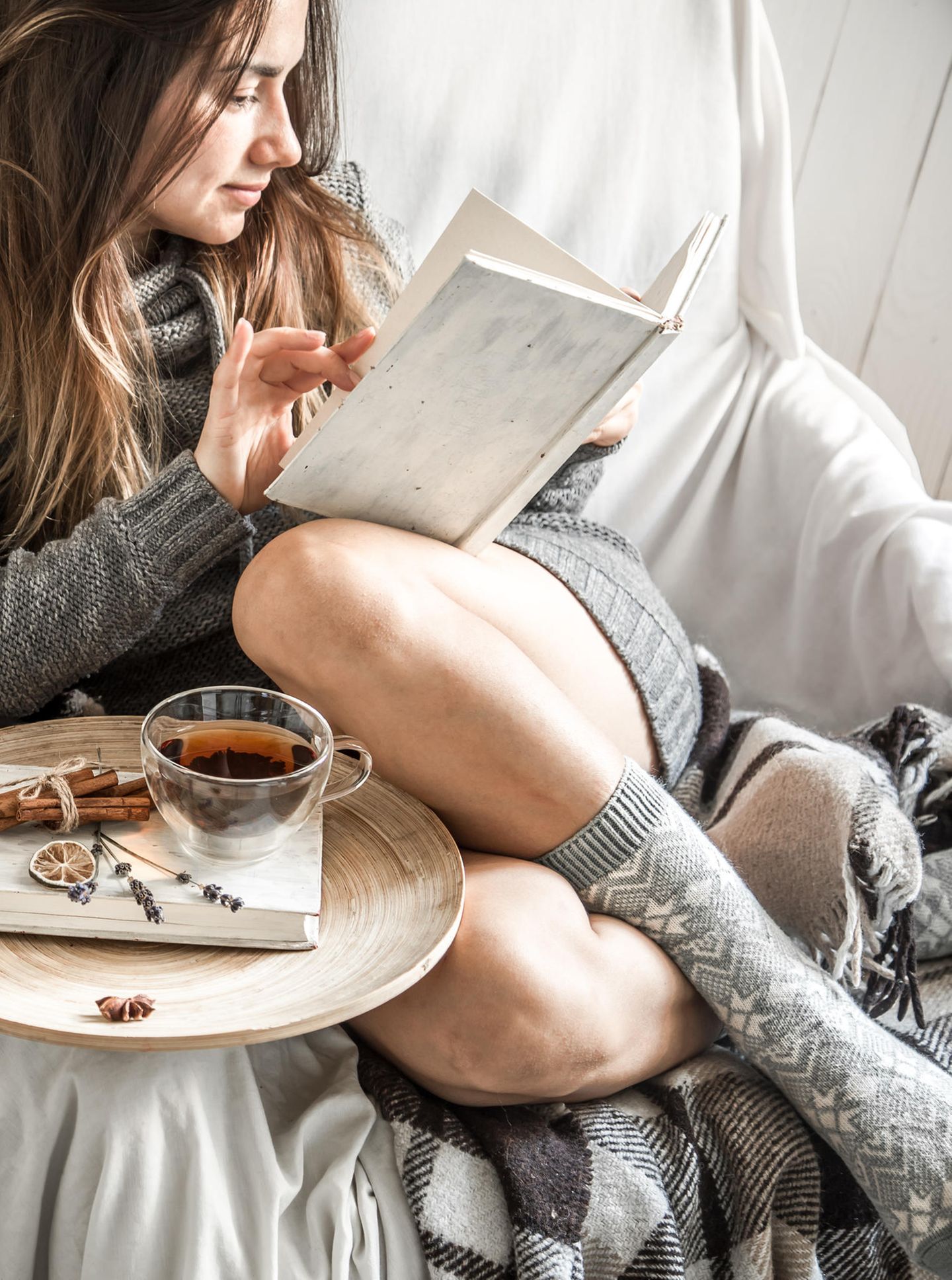 Herbst-Ideen: Frau sitzt auf Sofa mit einer Tasse Tee und liest ein Buch