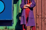 Frau trägt rotes Outfit mit violettem Mantel darüber