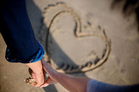 Was Männer wollen: Frauenhand greift Männerhand über einem Herz im Sand