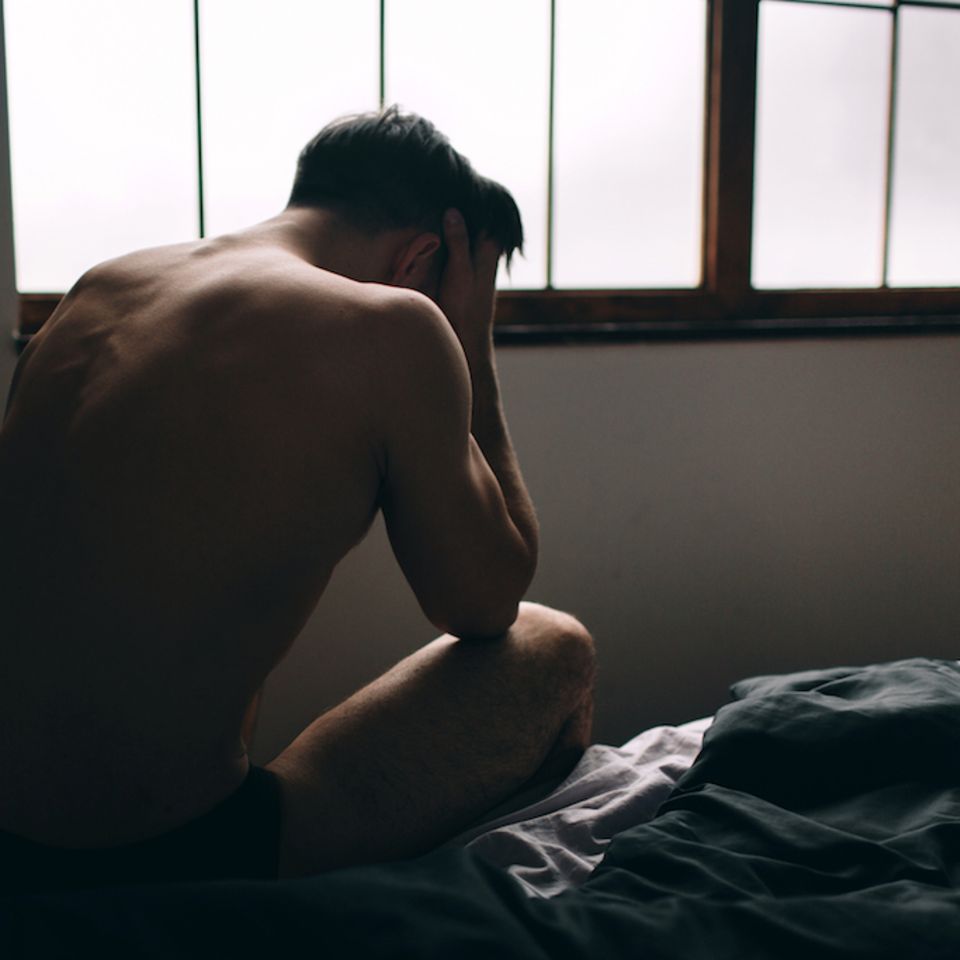 Sexsucht bei Männern: Mann sitzt verzweifelt auf Bett