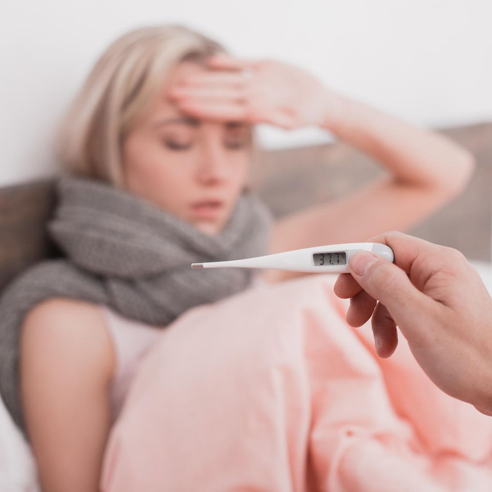 Hausmittel gegen Fieber: Frau mit Fieber und ein Thermometer