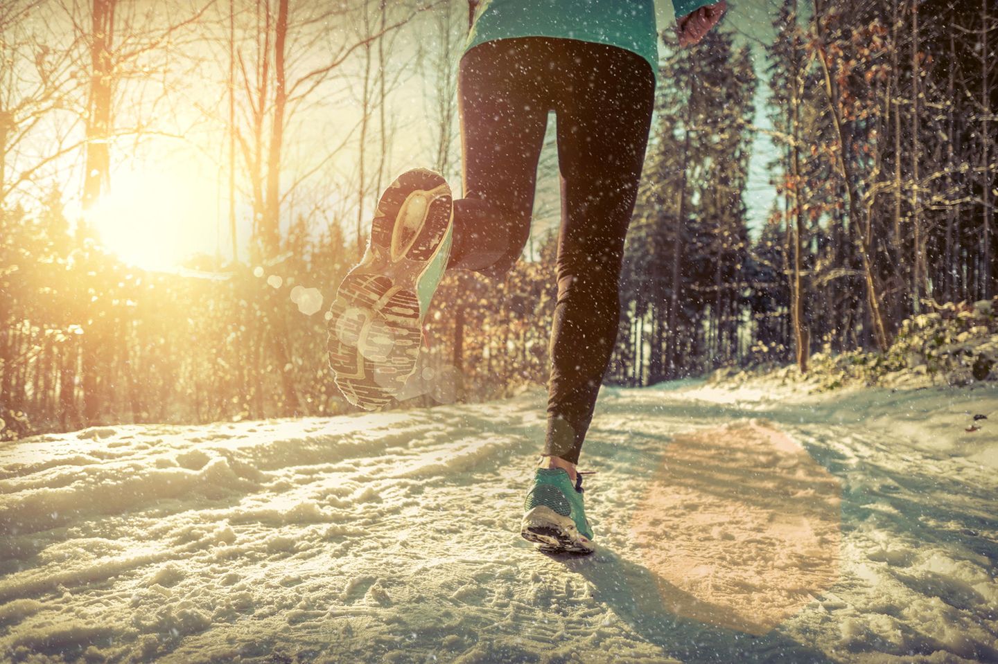 Joggen im Winter: Eine Frau joggt über einen schneebedeckten Waldweg