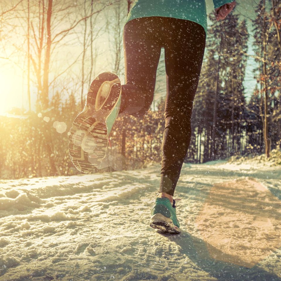 Joggen im Winter: Eine Frau joggt über einen schneebedeckten Waldweg