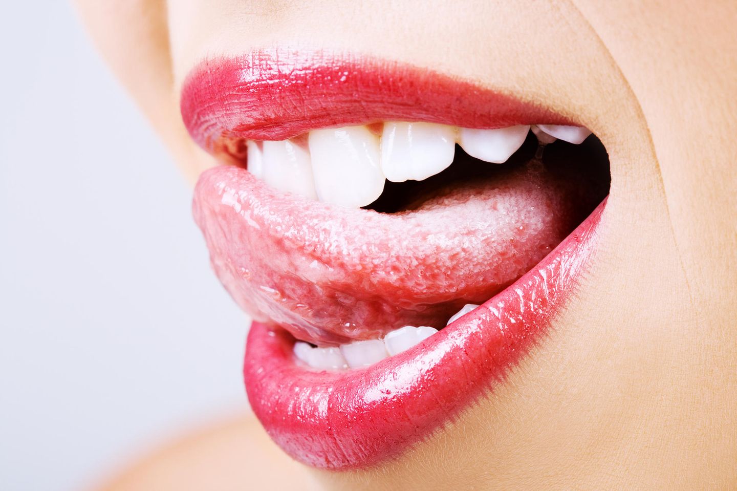 Pickel auf der Zunge: Frau streicht mit Zunge über die Zähne