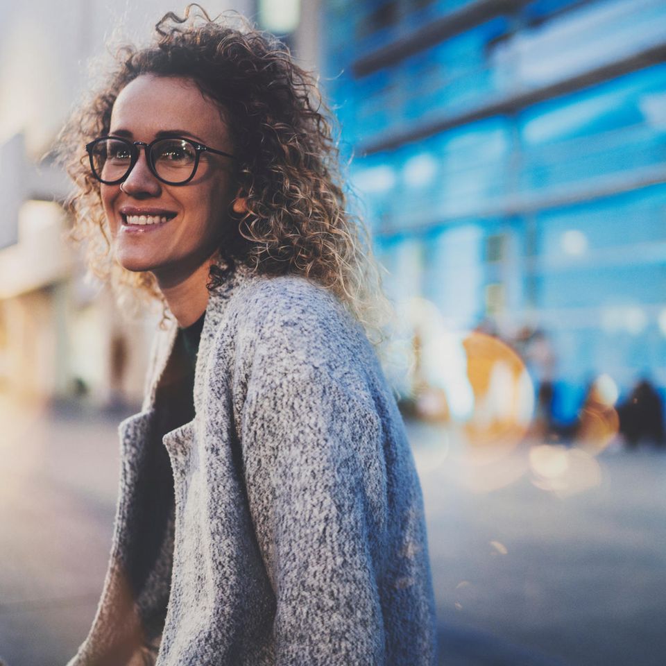 Authentisch sein: Eine lächelnde lockige Frau mit Brille vor einem modernen Bürogebäude