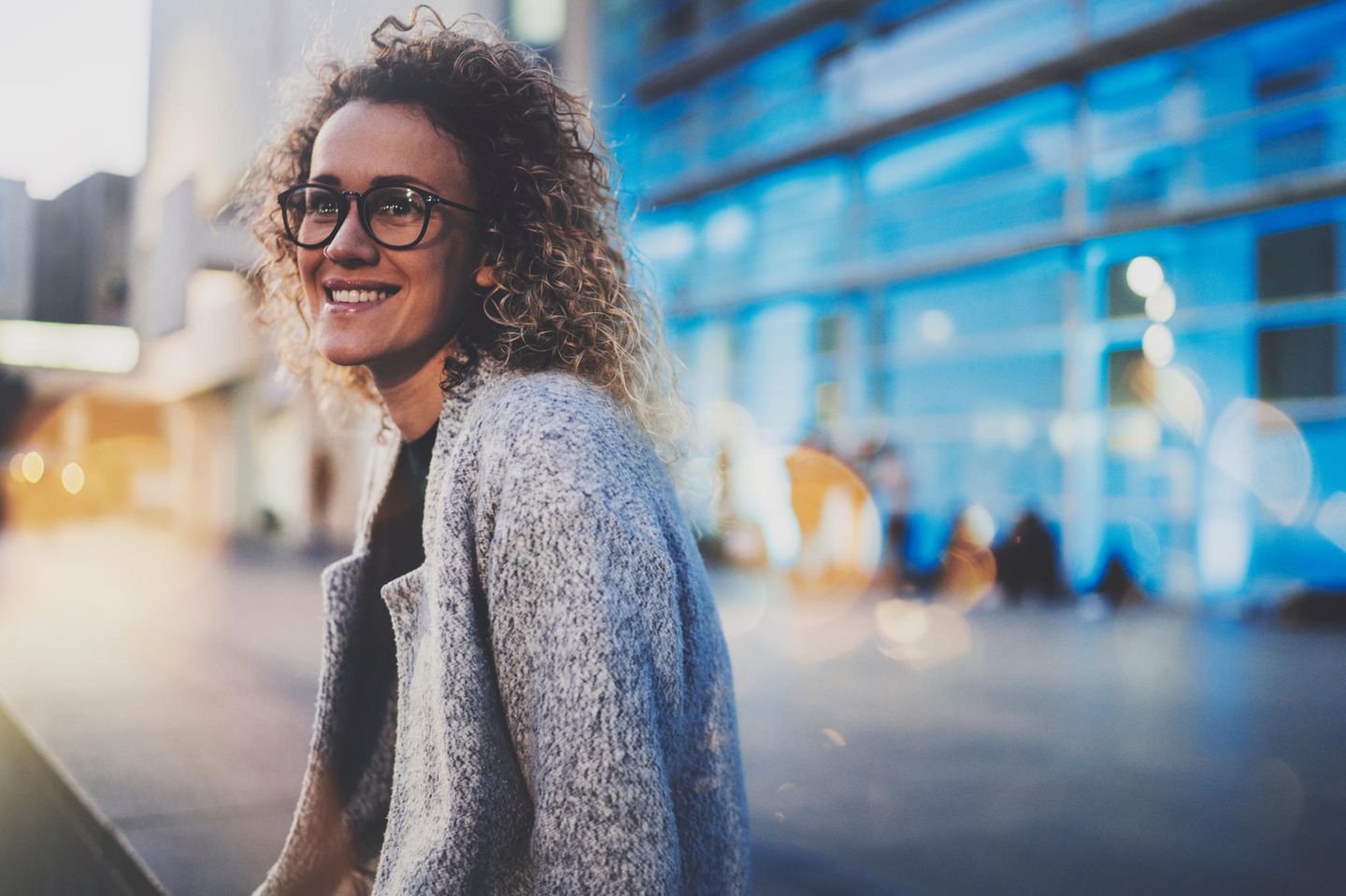 Authentisch sein: Eine lächelnde lockige Frau mit Brille vor einem modernen Bürogebäude