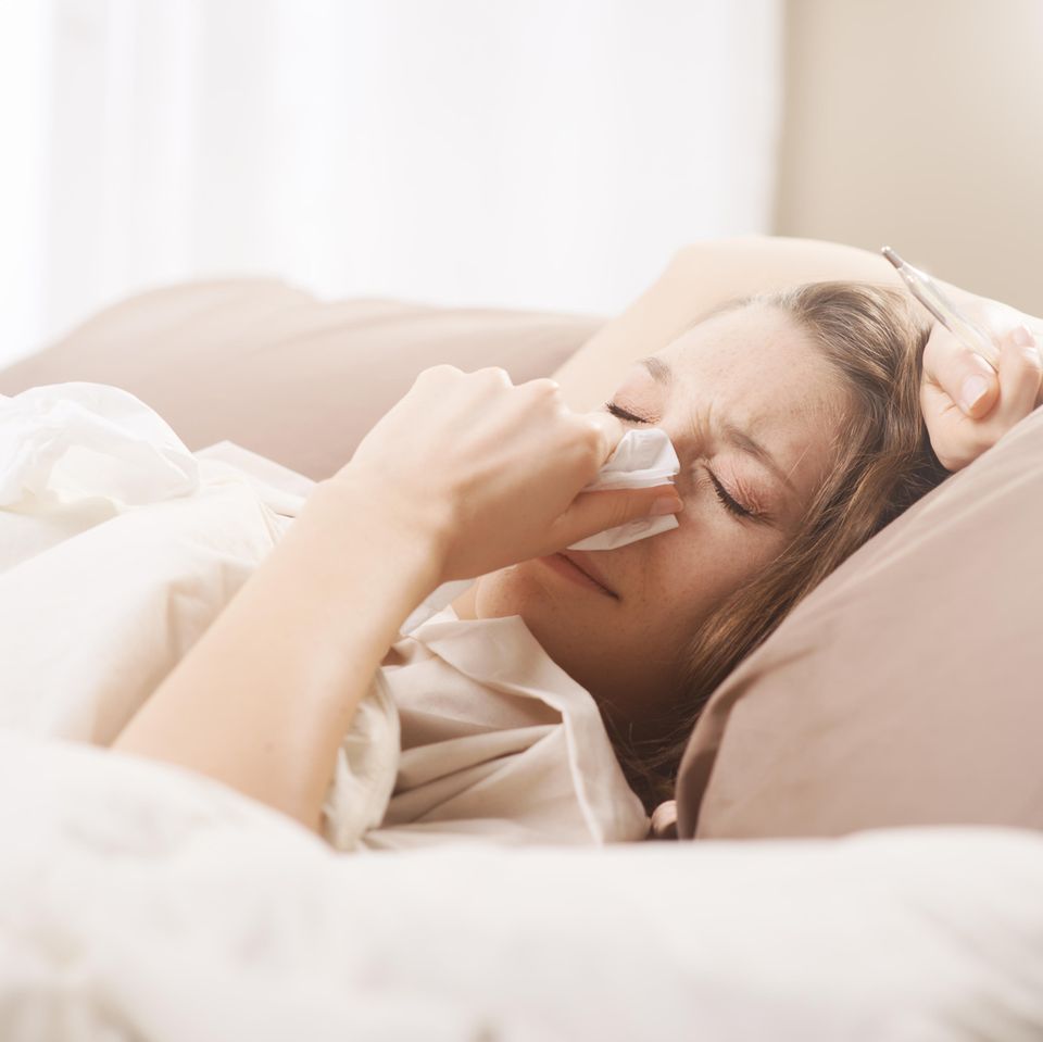 Grippe Dauer: Frau liegt krank im Bett