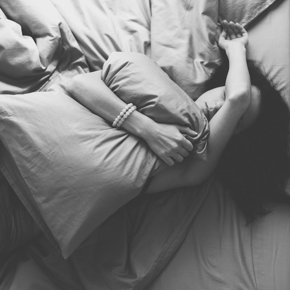 Premenstruelle Dysphorie: Frau verzweifelt auf Bett mit Kissen