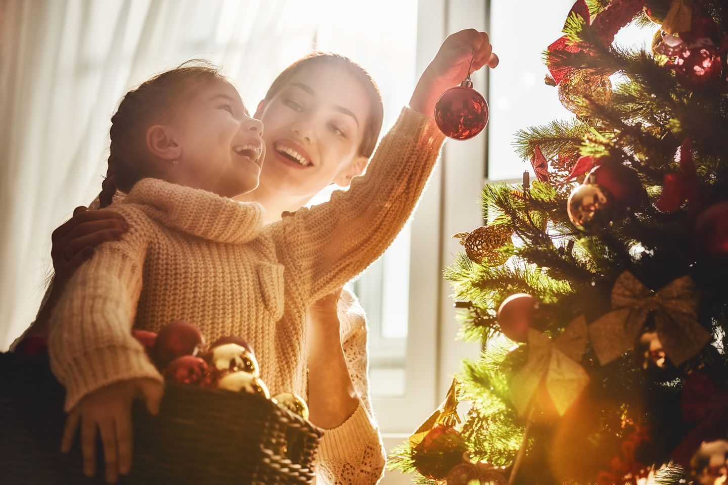 Weihnachtsbaum aufstellen: Mutter und Tochter hängen Kugeln an den Baum