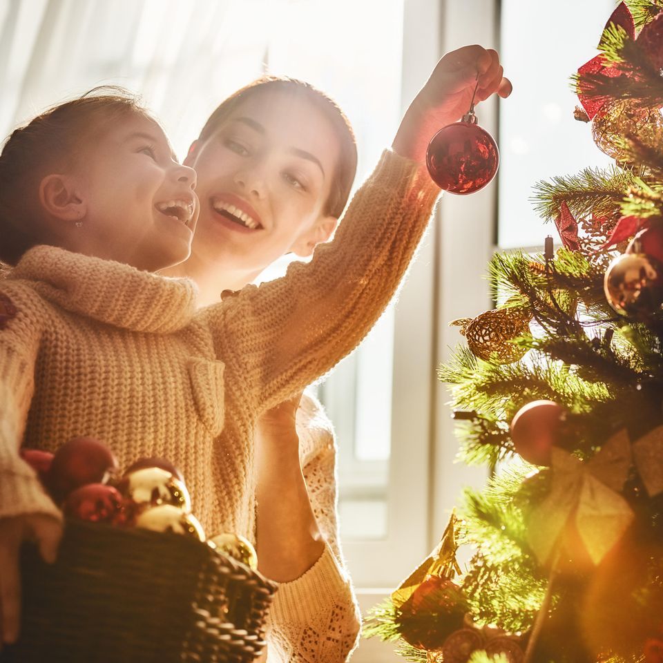 Weihnachtsbaum aufstellen: Mutter und Tochter hängen Kugeln an den Baum