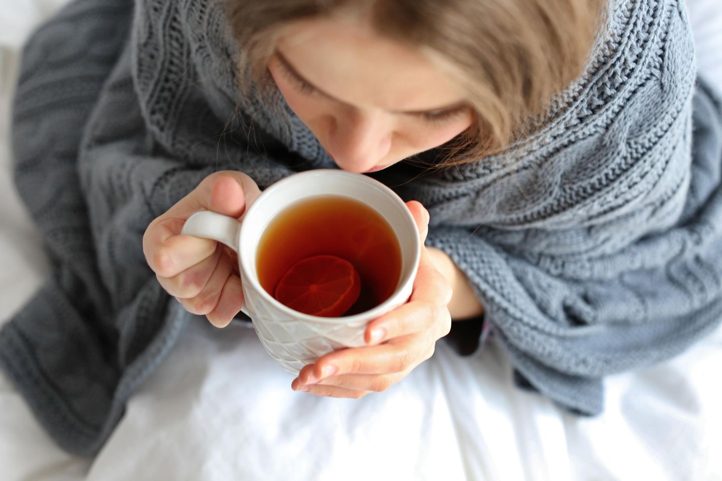 Hausmittel bei Blasenentzündung: Frau in Decke eingehüllt trinkt eine Tasse Tee
