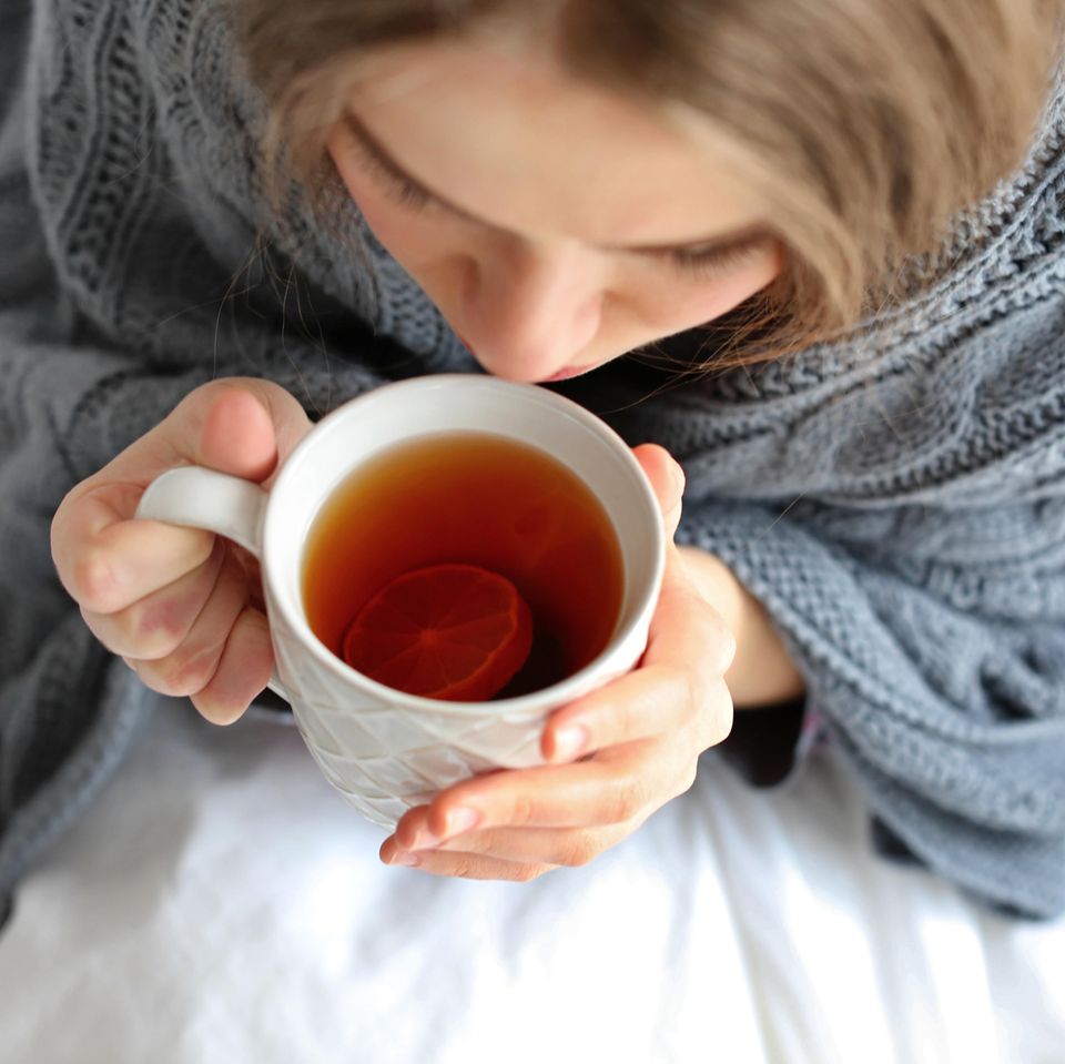 Hausmittel bei Blasenentzündung: Frau in Decke eingehüllt trinkt eine Tasse Tee