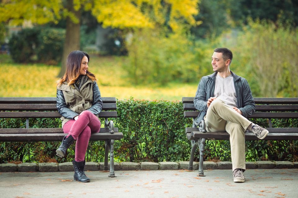 Frauen ansprechen: Ein Mann und eine Frau sitzen auf zwei Parkbänken und schauen sich an