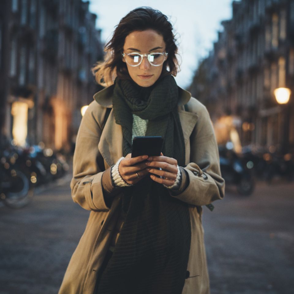 Digitale Abhängigkeit: Frau steht auf einer Straße und schaut auf ihr Handy