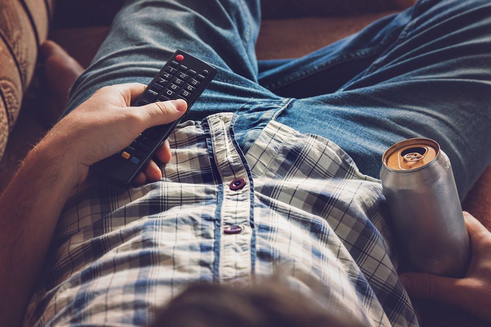 Partner lässt sich gehen: Mann der mit Biersode in der Hand vorm Fernseher sitzt