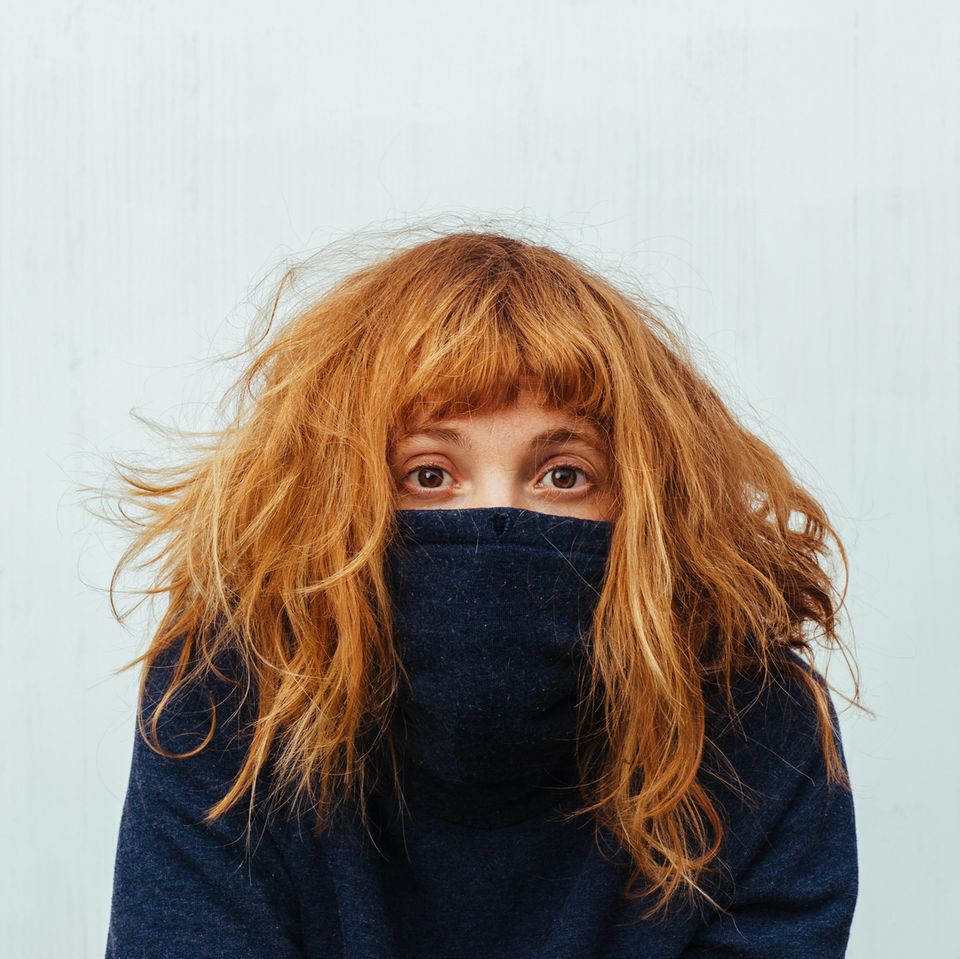 Anzeichen, dass du dich selbst nicht liebst: Eine junge Frau versteckt sich unter ihrem Pulli