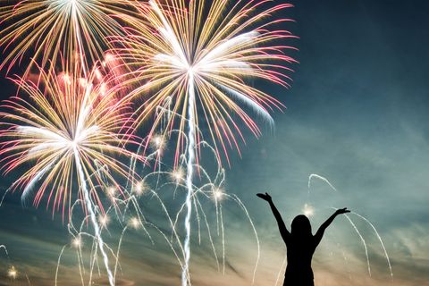 Silvesterwünsche für Familie, Freunde und Kollegen: Frau beobachtet Feuerwerk und streckt Arme in die Luft