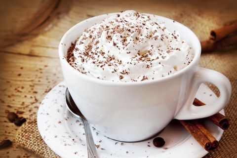 Weihnachtskaffee: So leicht geht das leckere Wintergetränk: Tasse gefüllt mit Kaffee und Sahnehaube, daneben Zimtstangen