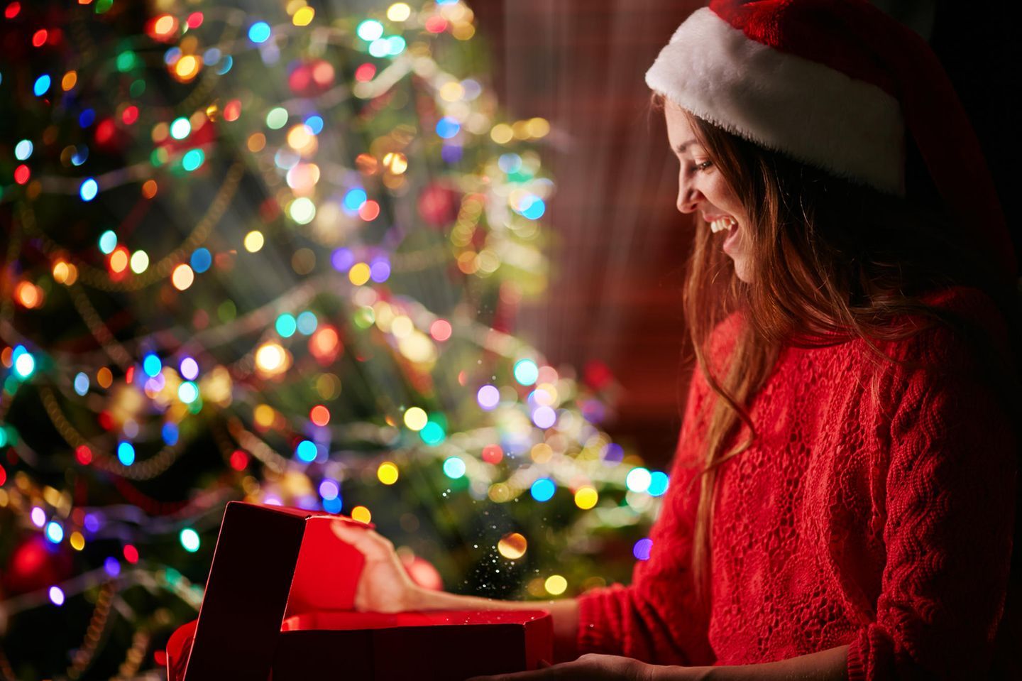 Geschenke für mich selbst: Frau öffnet Geschenk am Weihnachtsbaum