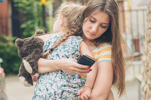 Freizeitplanung fürs Kind: Frau trägt Kind im Arm und schreibt am Smartphone