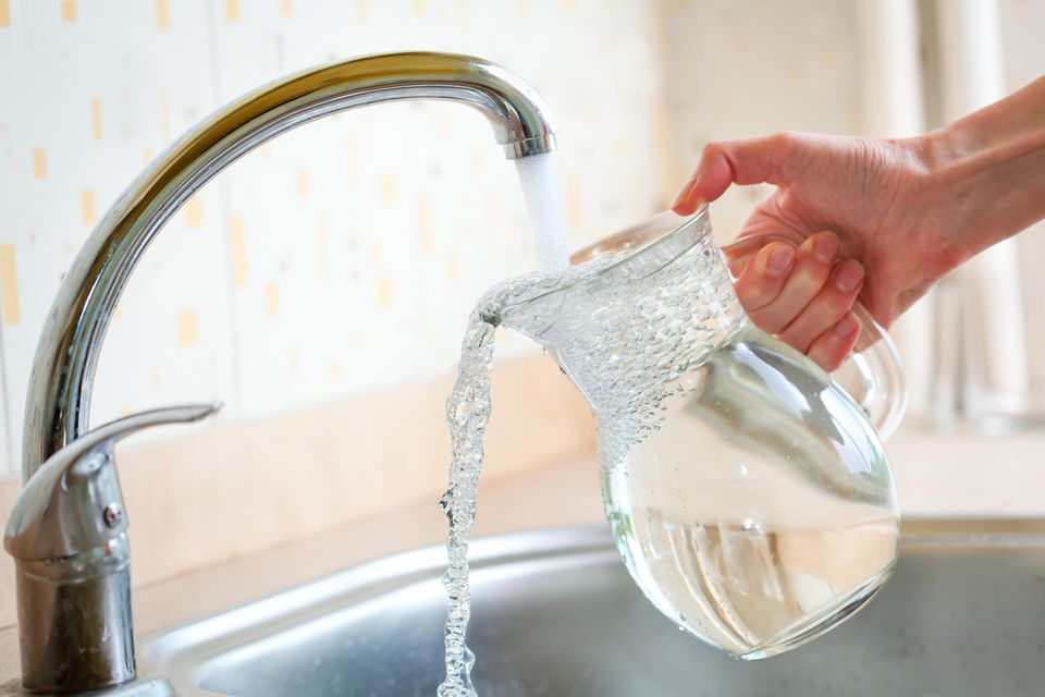Leitungswasser trinken: Ist das wirklich gesund? Fließendes Wasser aus dem Hahn, das in eine Karaffe läuft