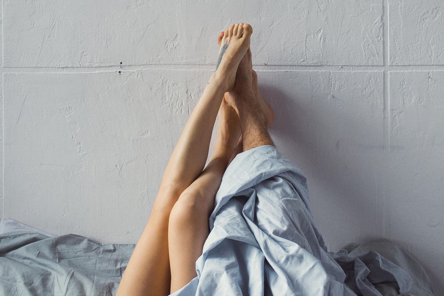 Apfelstrudel-Stellung: Frauenbeine und Männerbeine gucken unter der Bettdecke hervor