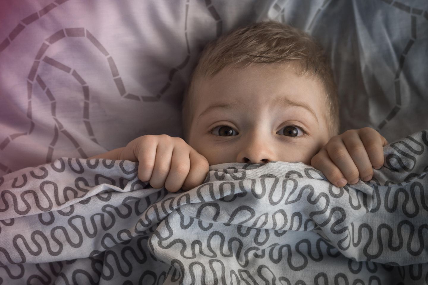 10 Kinderängste und 5 Lösungen: Junge schaut ängstlich unter der Bettdecke hervor