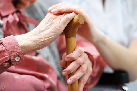 Pflegerin streichelt Hand einer alten Frau