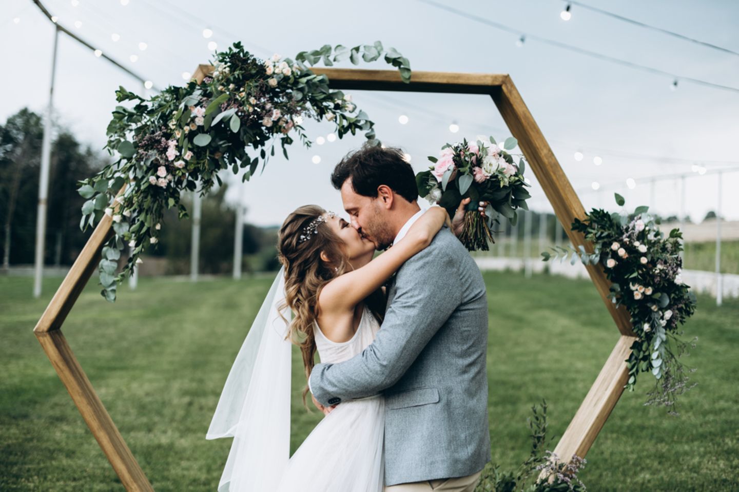 Hochzeitstrends 2019: Diese 6 werdet ihr lieben: Hochzeitspaar küsst sich vor einem geschmückten Holzbogen