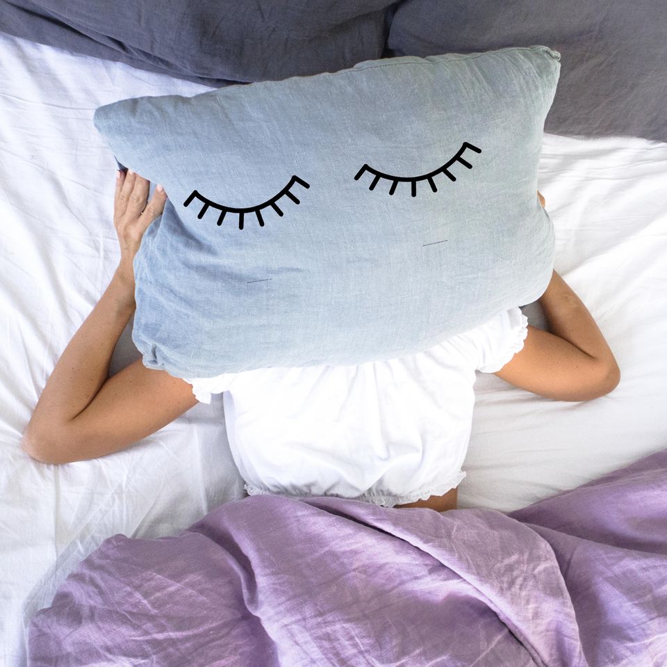 Augenschatten: Frau liegt im Bett und hält Kissen über dem Kopf